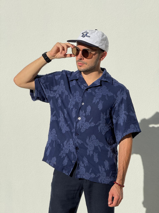 Man wearing a navy patterned Parce shirt and cap against a light background