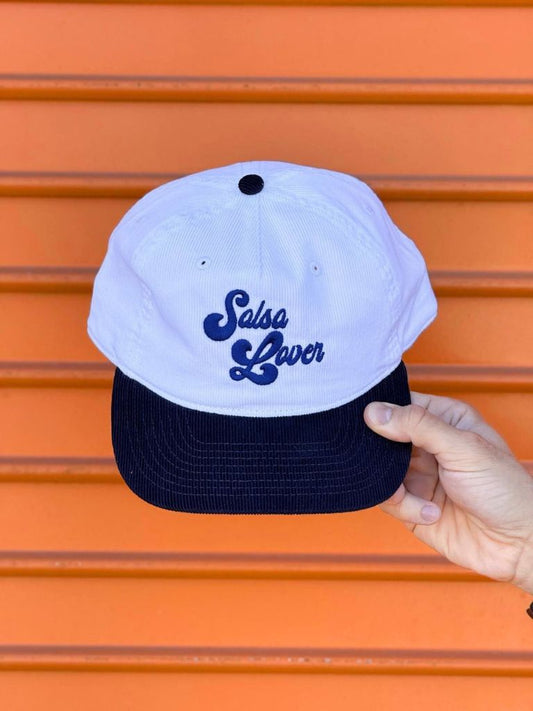 White cap with blue text held by a hand against an orange background