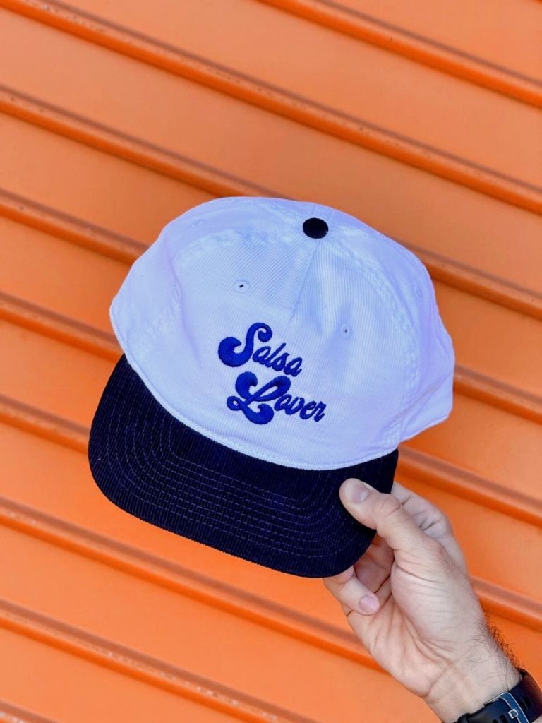 White cap with blue text held by a hand against an orange background