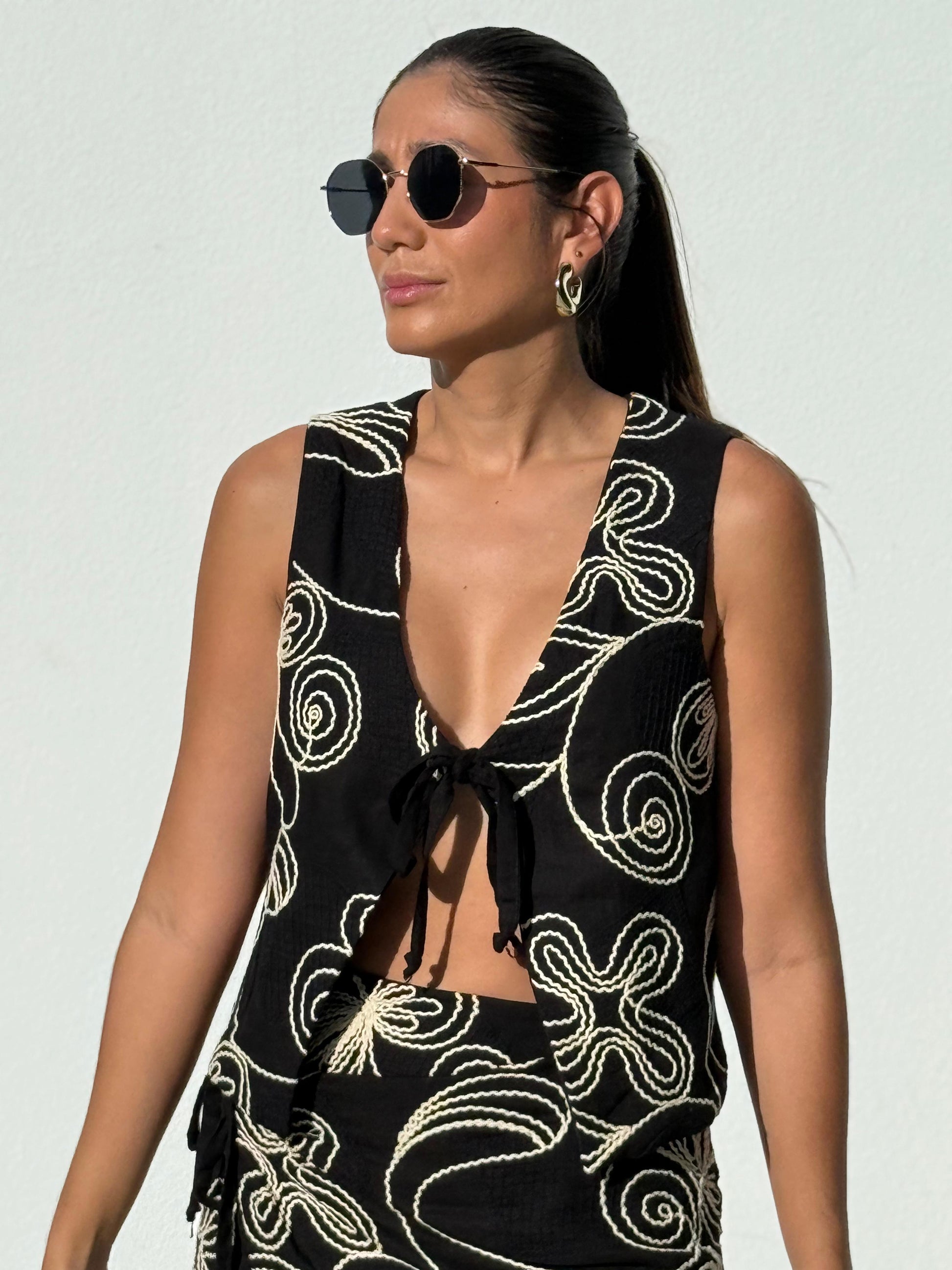 Woman wearing the Flor de Noche embroidered cotton vest by Parce Miami – black sleeveless top with ivory floral embroidery, handmade in Colombia.